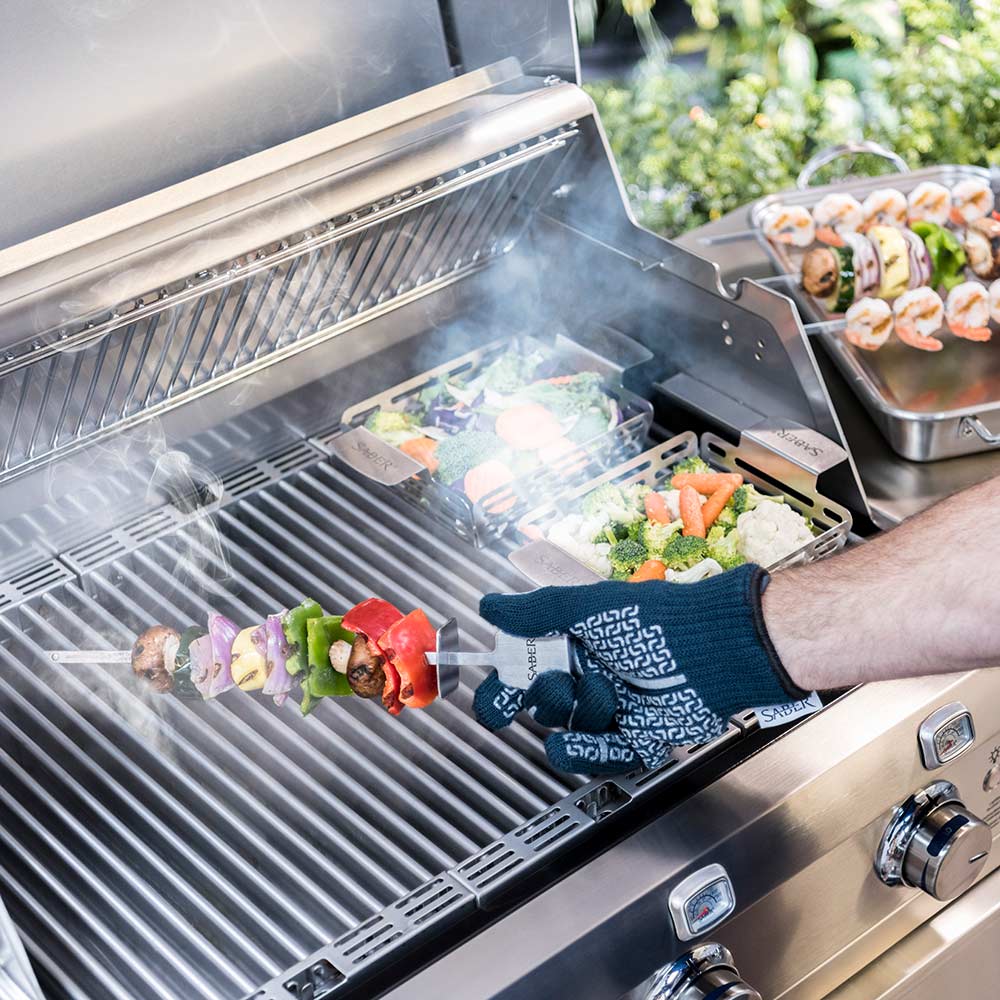 Saber grill set in use with metal cooking baskets, skewers, and gloved handling