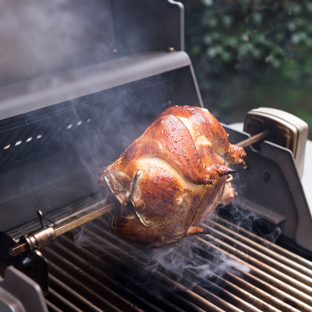 Rotisserie spit rod holding a whole roast chicken on a 2-burner grill