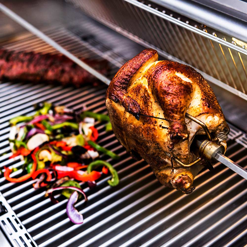 Rotisserie rod with chicken attached over grill grates