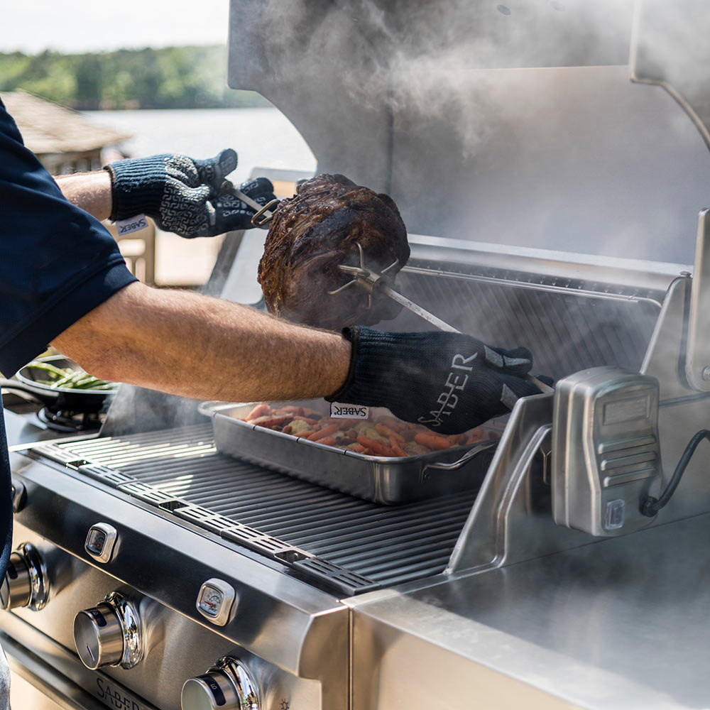 Rotisserie rod with whole chicken turning beside grill fire