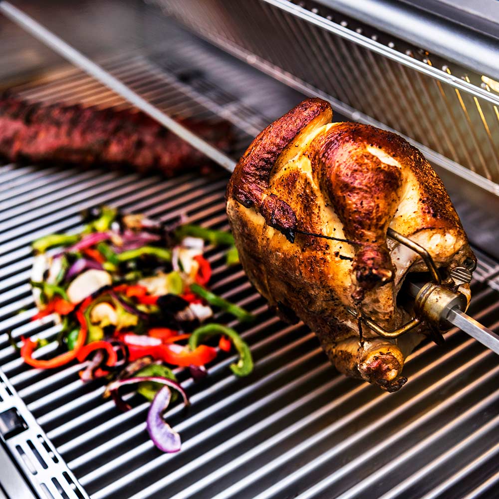 Rotisserie rod with cooked chicken on grill grates