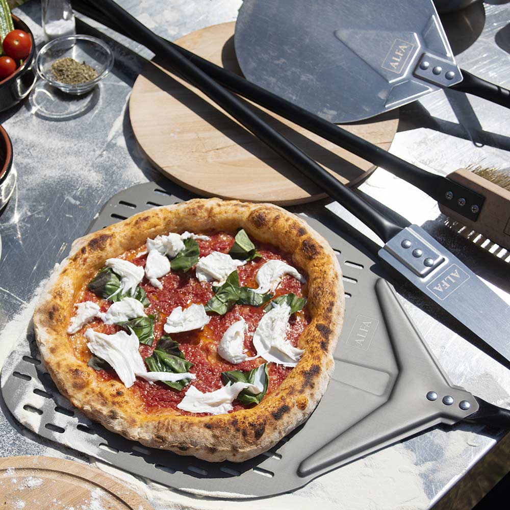 Pizza peel lifting a topped pizza from a perforated metal pizza stone surface