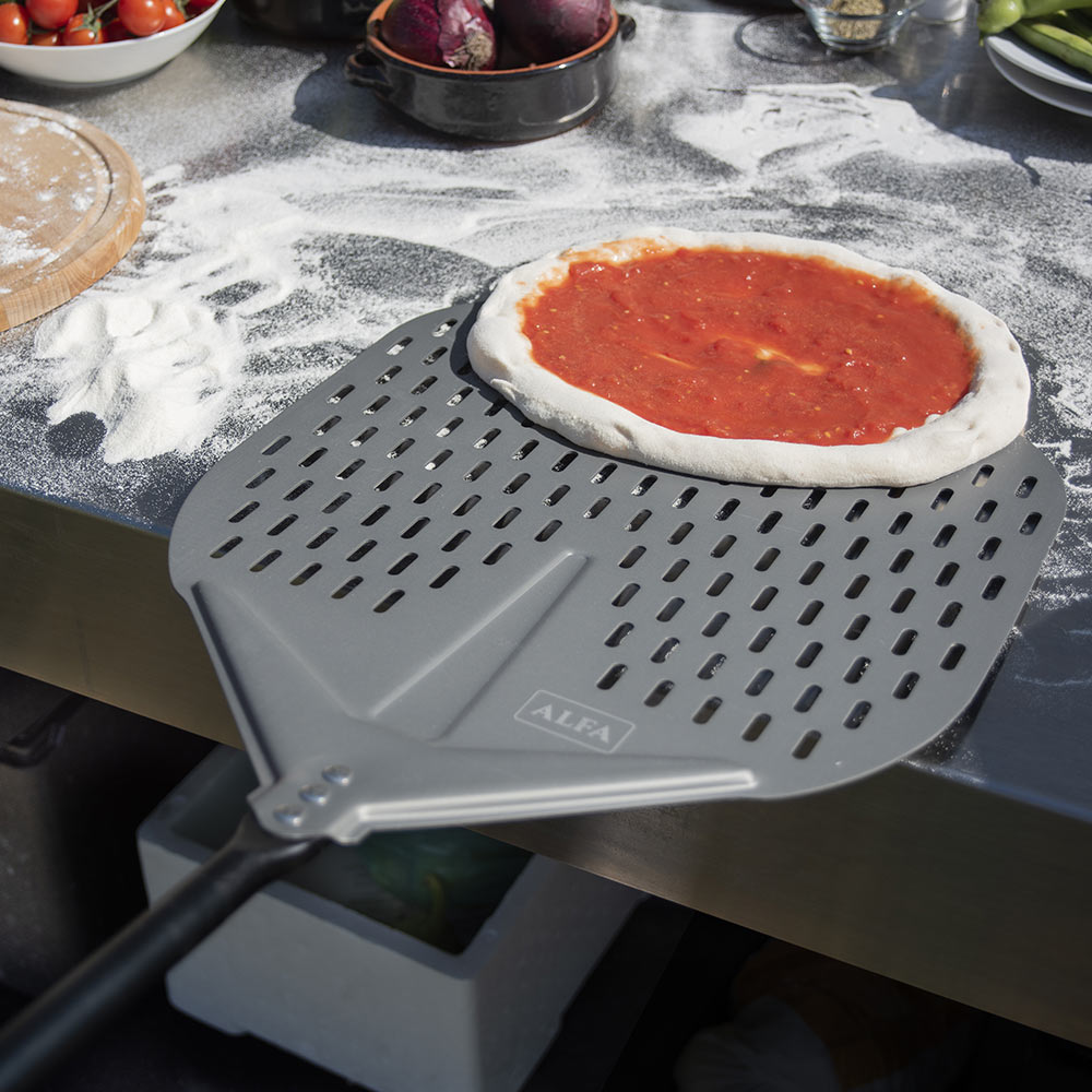 Gray perforated pizza shovel holding a sauce-topped pizza on a metal tray