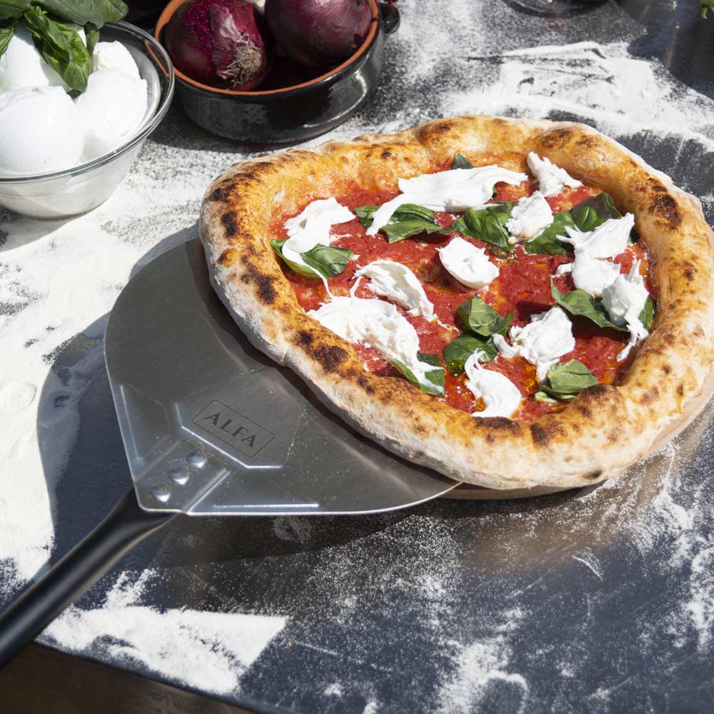 Pizza turner sliding under topped pizza on a floured prep surface