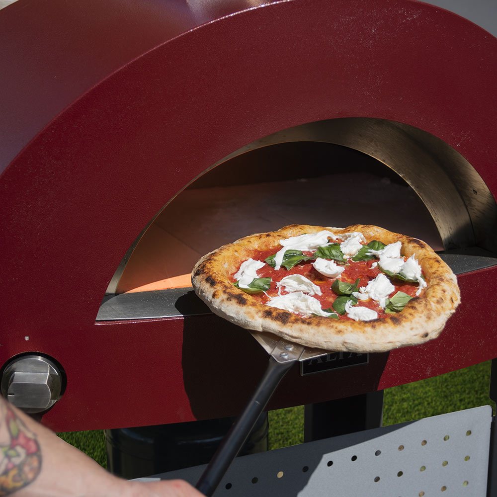 Pizza peel sliding topped pizza into a red pizza oven
