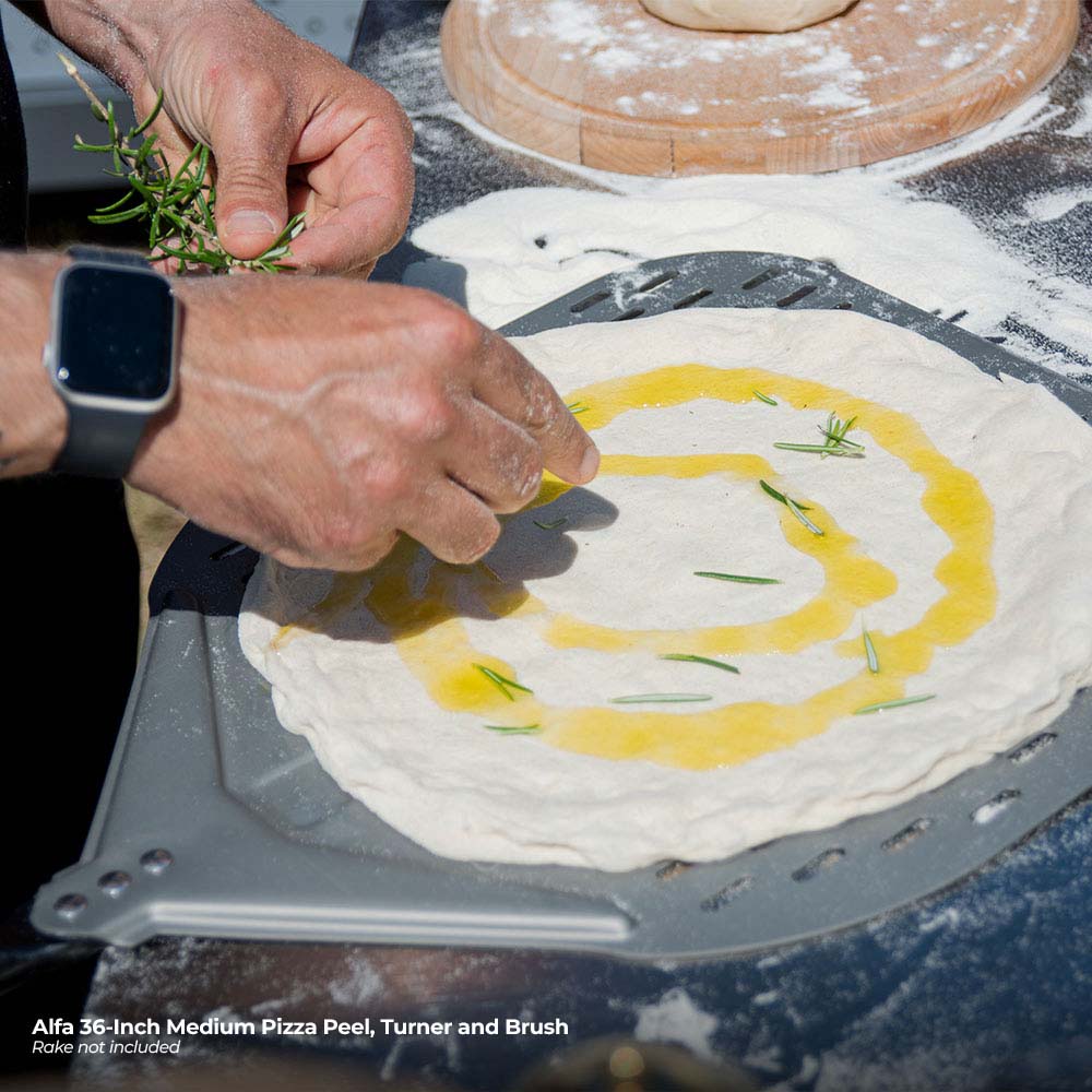 Perforated pizza peel carrying dough with oil and scattered herbs