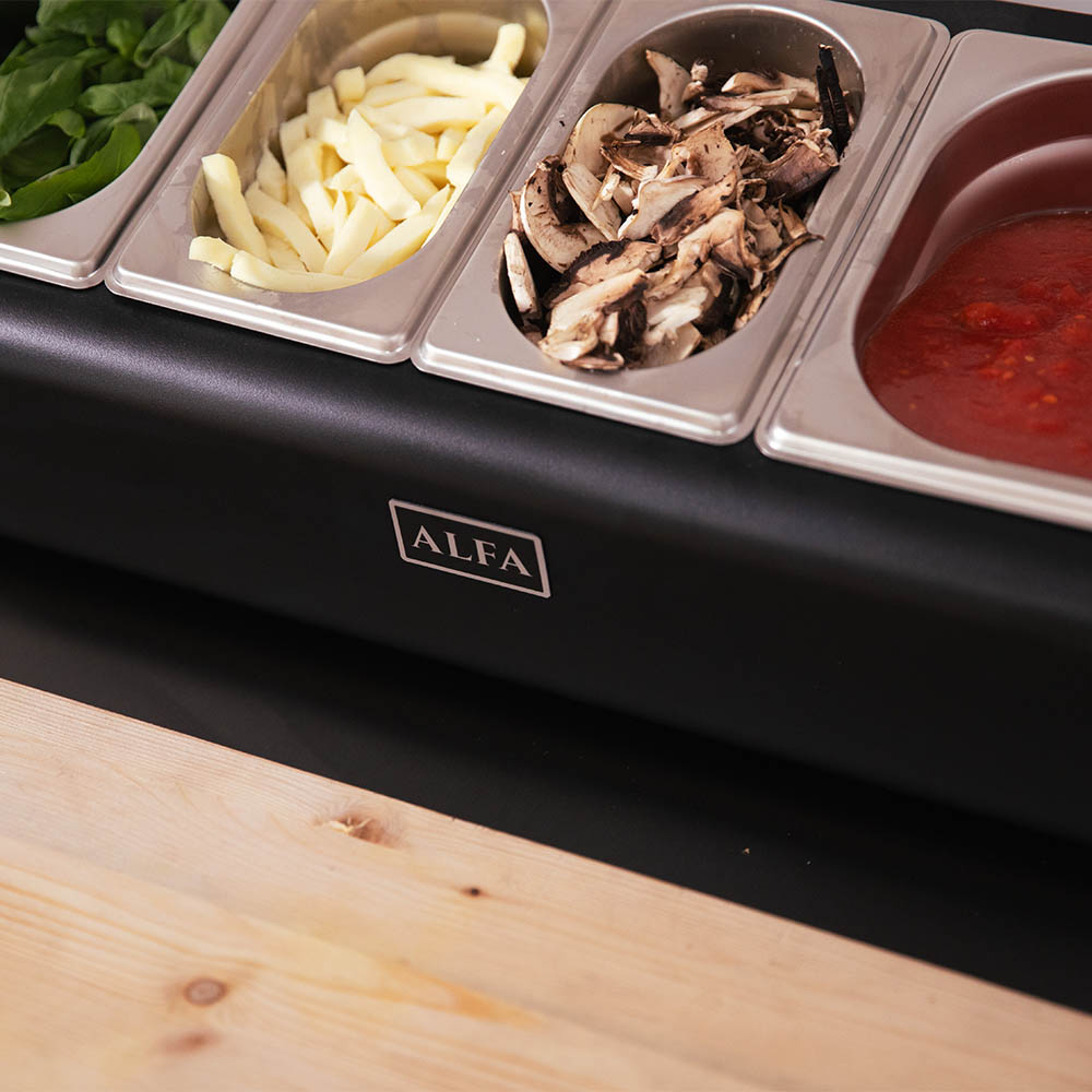 Topping station with four stainless compartments holding greens, onions, mushrooms, and red sauce