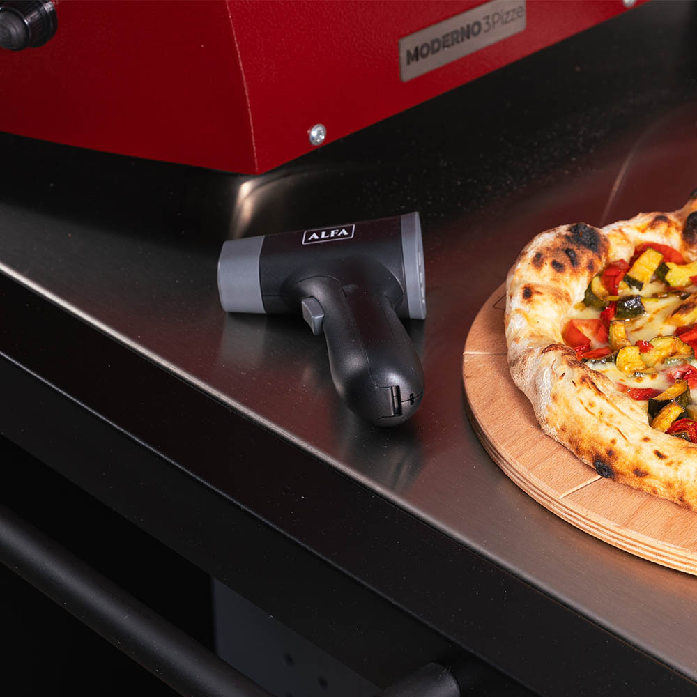 Handheld black laser thermometer with ALFA label, resting on oven front
