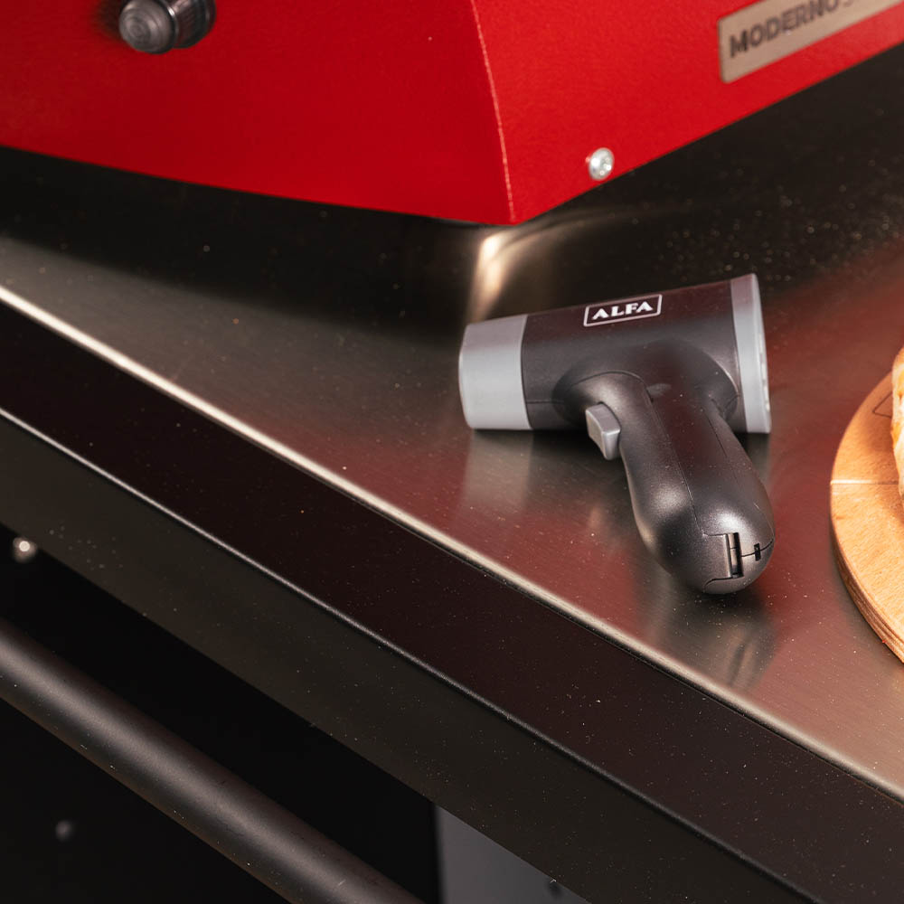 Handheld black laser thermometer resting on oven front with LCD facing up