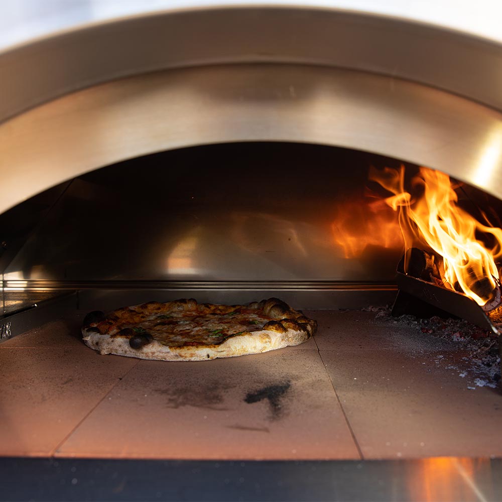 Pizza oven interior with pizza on stone and active flames along the back wall