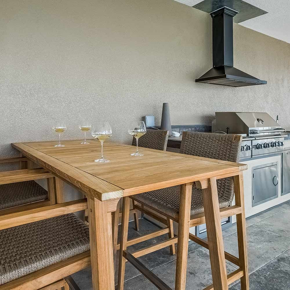 Counter-height teak dining table with woven chairs and square tabletop in light wood.