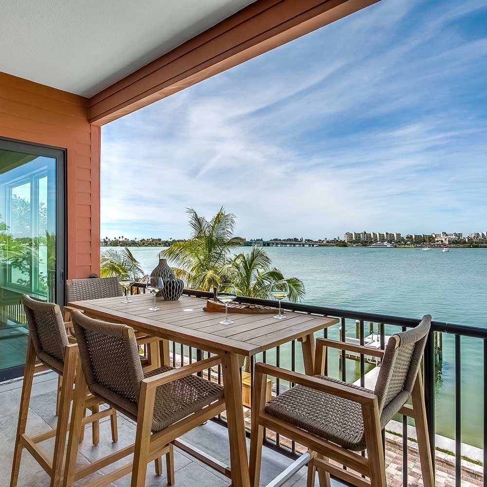Outdoor counter-height dining set with rectangular teak table and woven chairs on waterfront deck.