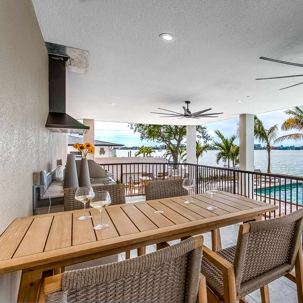 Teak counter-height table with slatted top and tapered legs under covered patio.