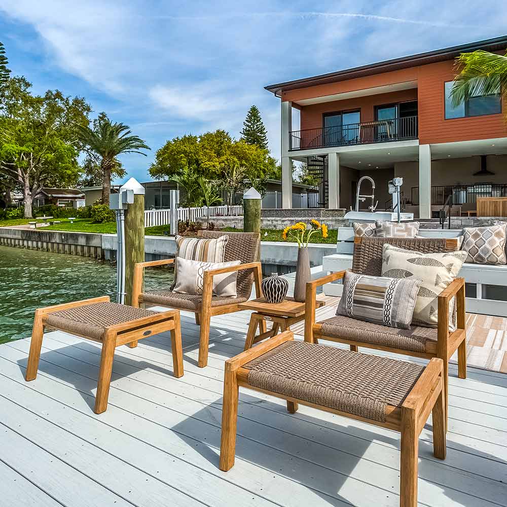 Outdoor furniture set on a deck by a waterfront with a house in the background.