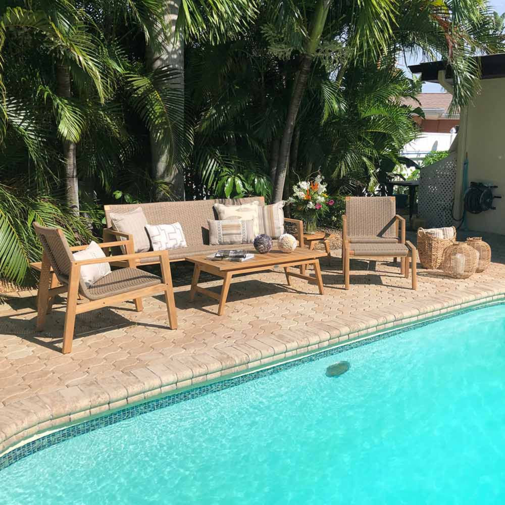 Outdoor patio seating set by a pool with light wood frames and tan cushions, including chairs