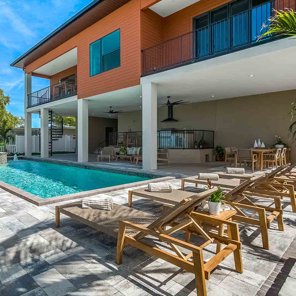 Outdoor lounge set with woven lounge chairs and a small teak coffee table by a pool