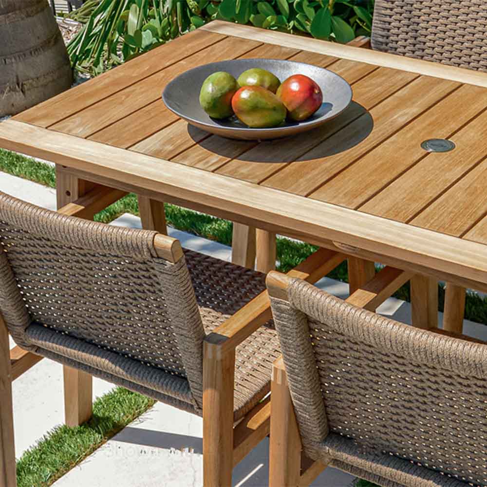 Rectangular teak dining table with woven chair arms and bowl of fruit centerpiece