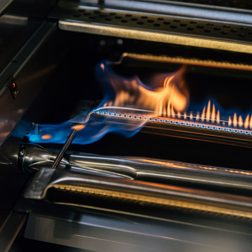 Gas grill burner with flames and metal spatula resting inside the cooking chamber.