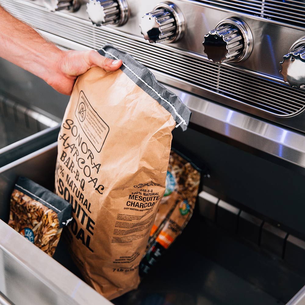 Freestanding grill cart with wood-stand shelf holding a bag of charcoal for grilling