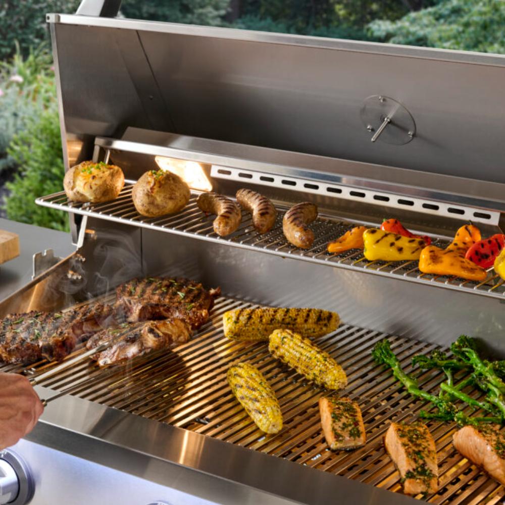 Open stainless built-in gas grill with racks holding potatoes, meat, and vegetables