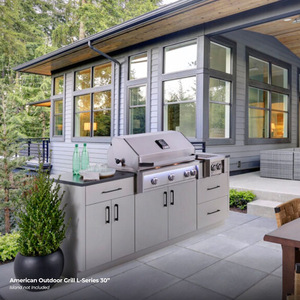 Stainless steel built-in gas grill with closed lid, four burner knobs, and cabinet doors