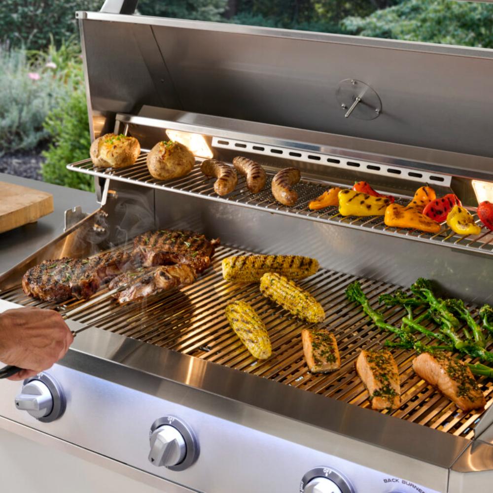 Open stainless steel gas grill with corn, vegetables, and burgers on the grates
