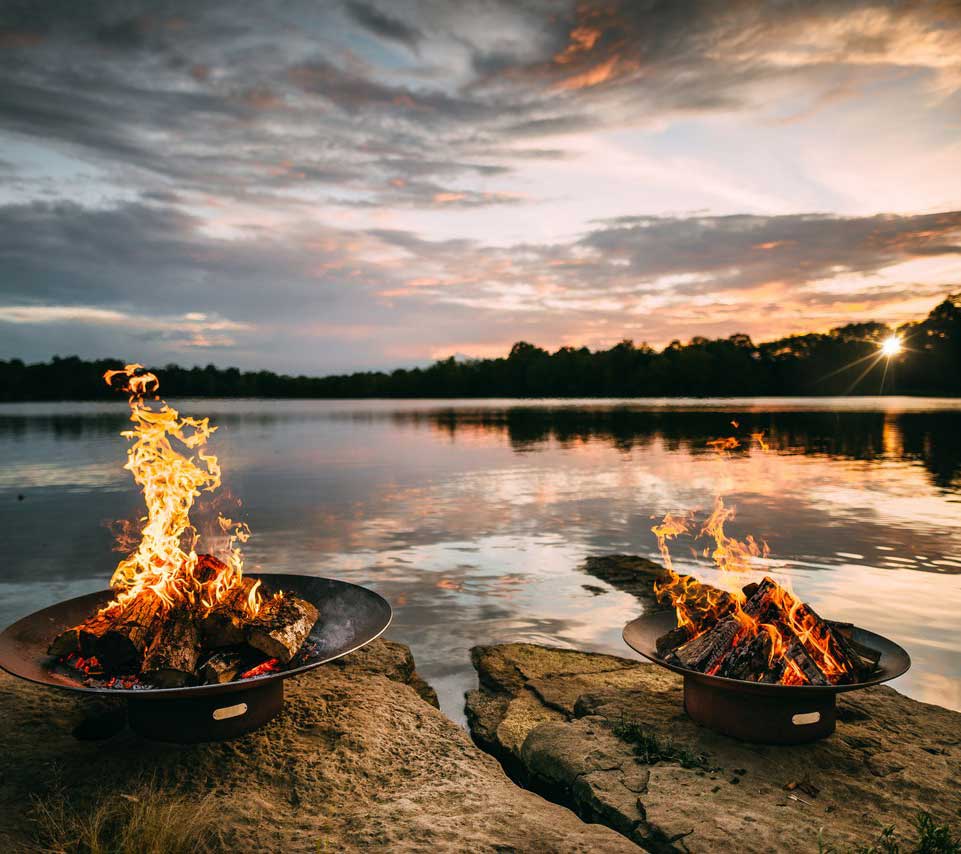 Multiple round wood fire pits with burning logs and flames at the rim