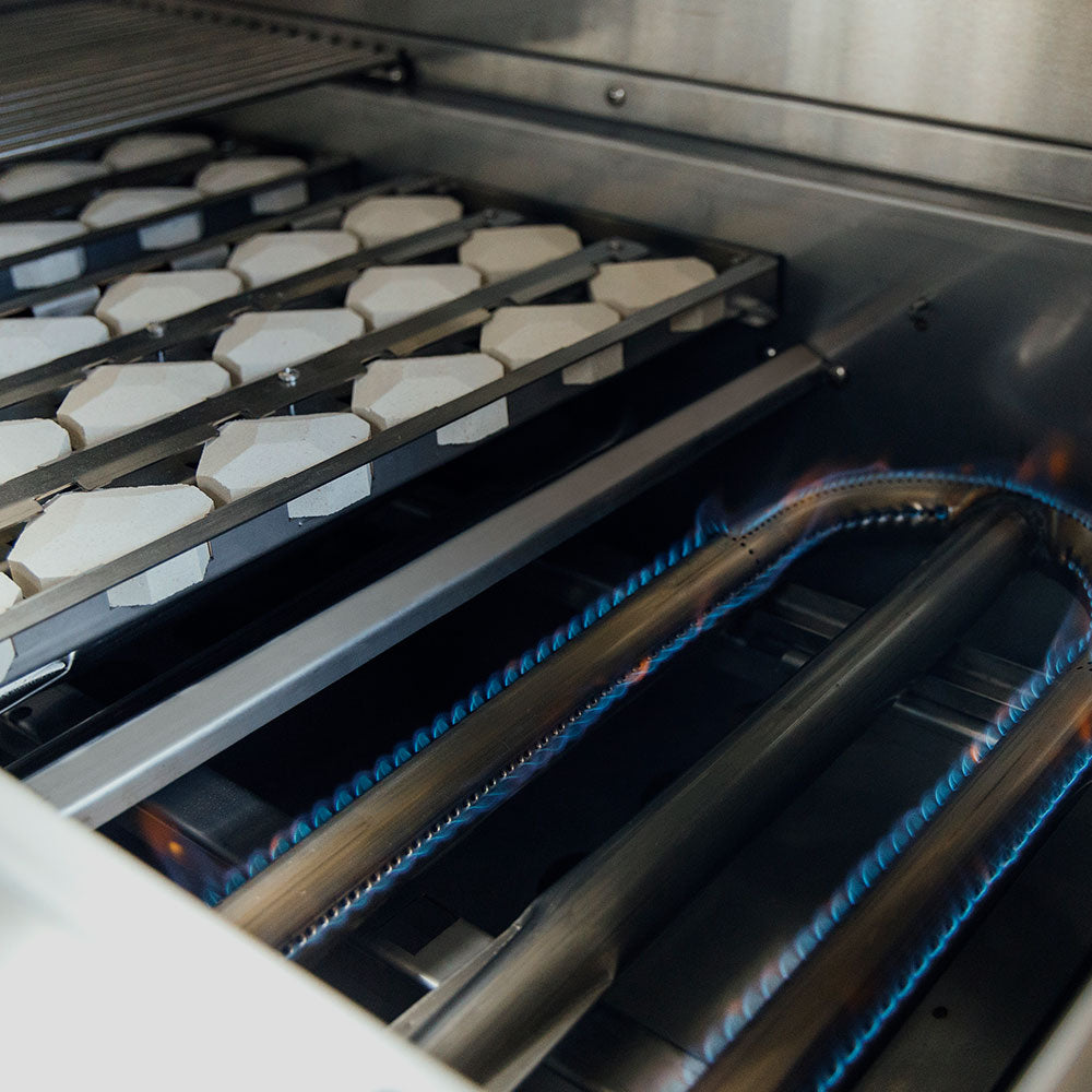 Gas grill burner tubes with blue glow under the cooking grate