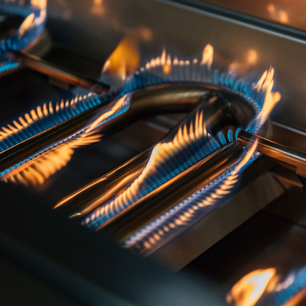 Close-up of gas grill burners with orange flames and blue-blue flame tips