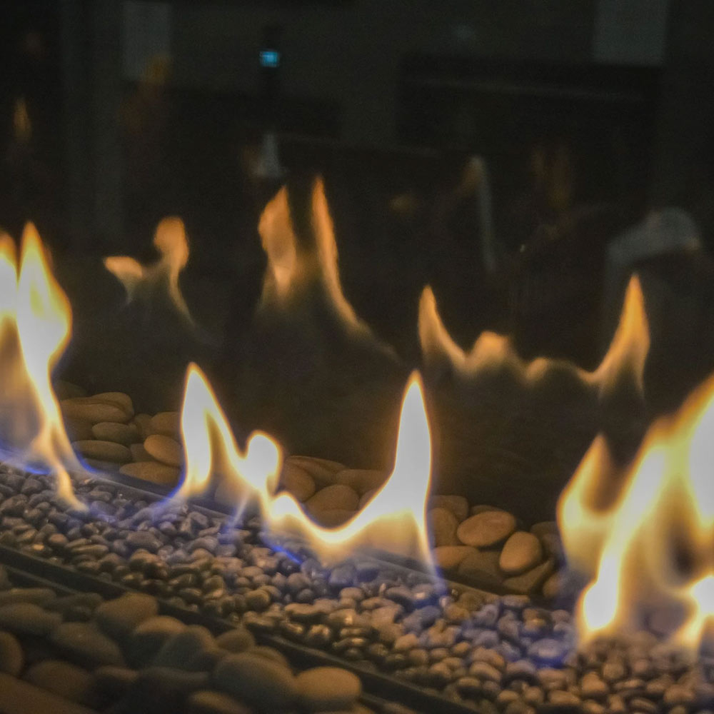 Close-up of gas flames burning over rock media inside a linear fireplace.