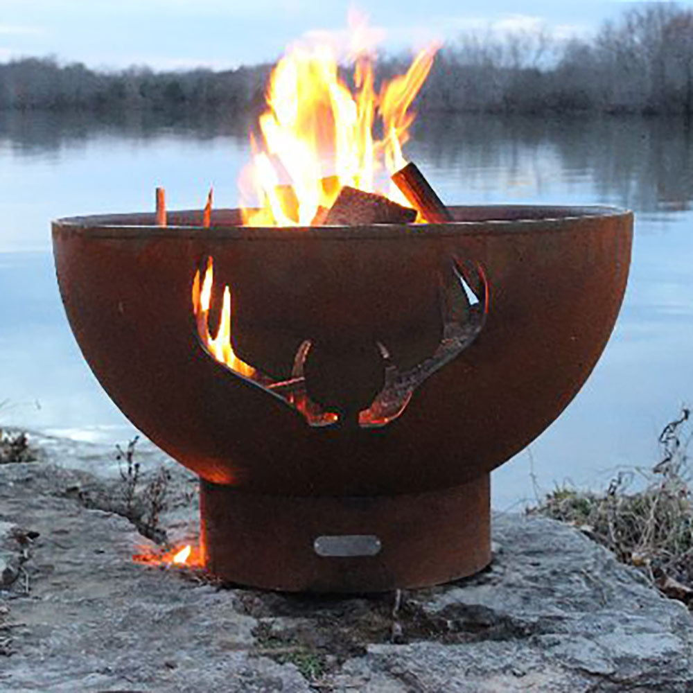 Outdoor steel fire pit bowl with antler-shaped openings and burning logs