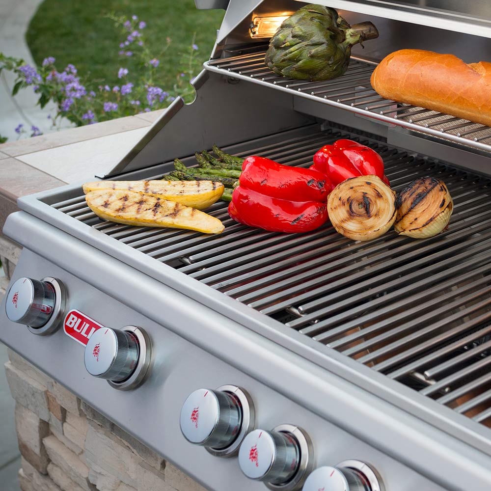 Built-in gas grill with mixed vegetables and peppers on stainless cooking surface