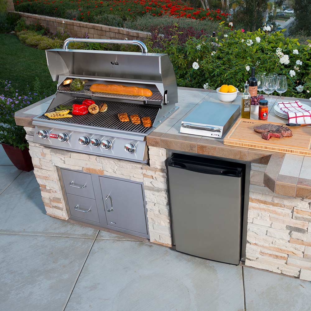 Outdoor built-in grill in a stone island with stainless cabinet doors and side shelf