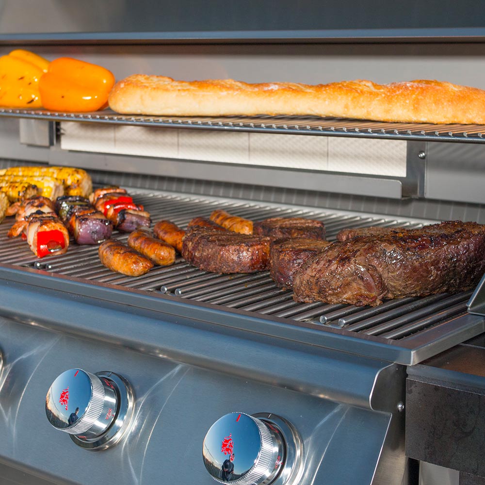 Gas grill cooking grates with grilled steaks, sausages, and vegetables