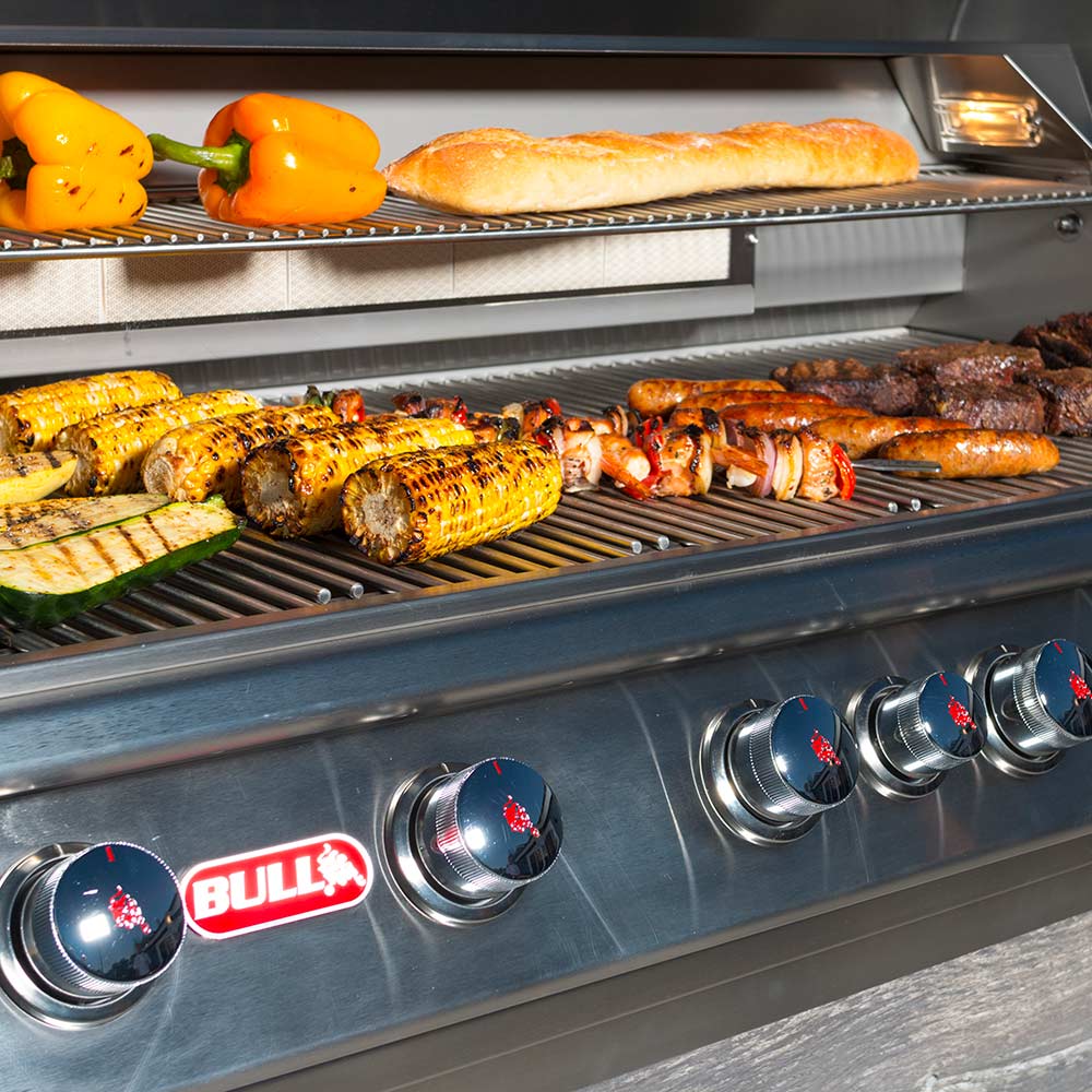 Gas grill cooking surface with grilled corn, peppers, and steaks; Bull control knobs