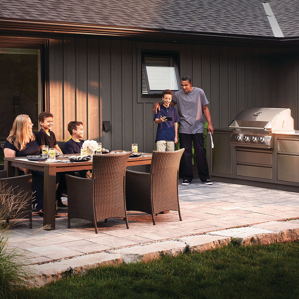 Stainless steel built-in gas grill head outdoors with lid and four front burner control knobs