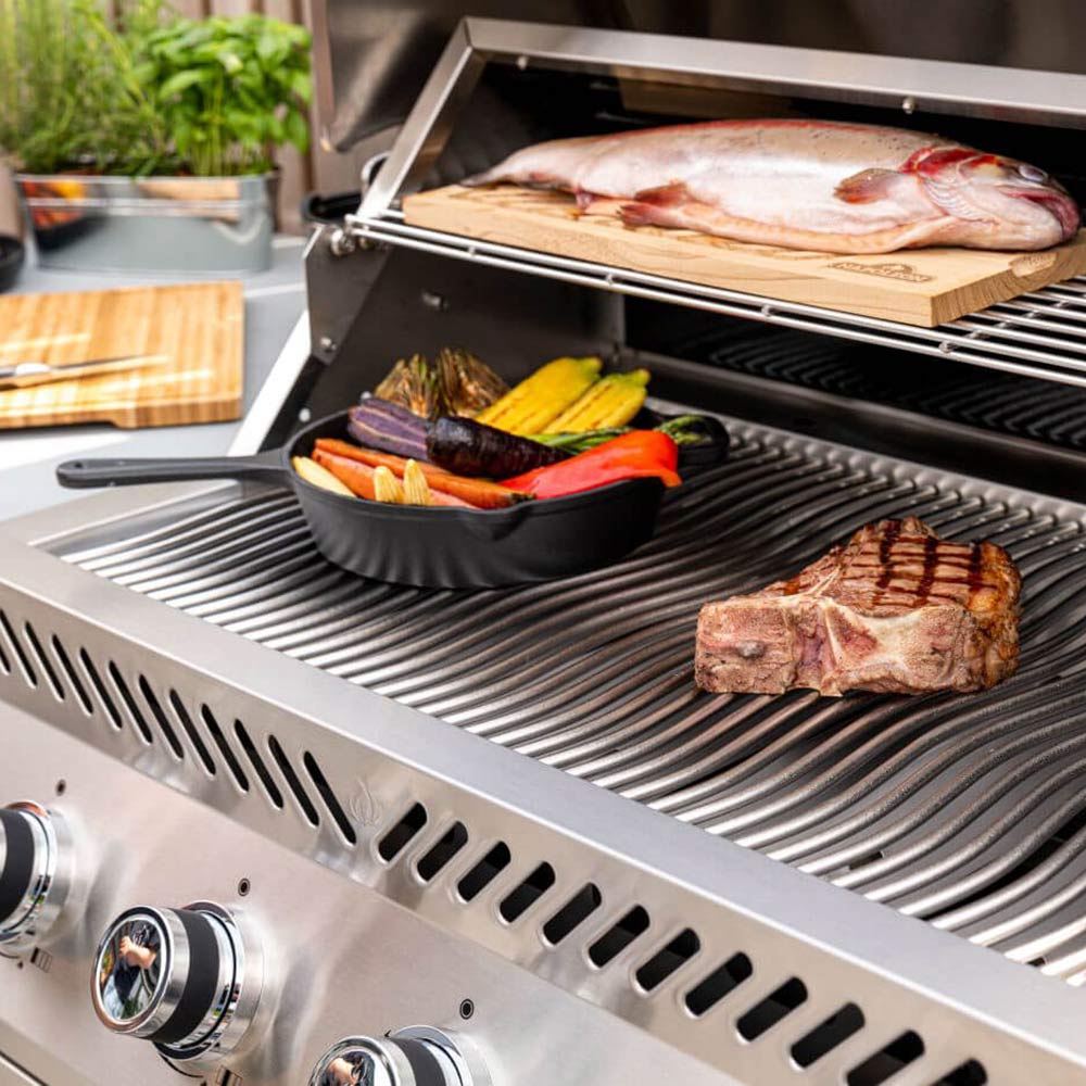 Open stainless steel grill with ribbed cooking grates and food on the burner surface
