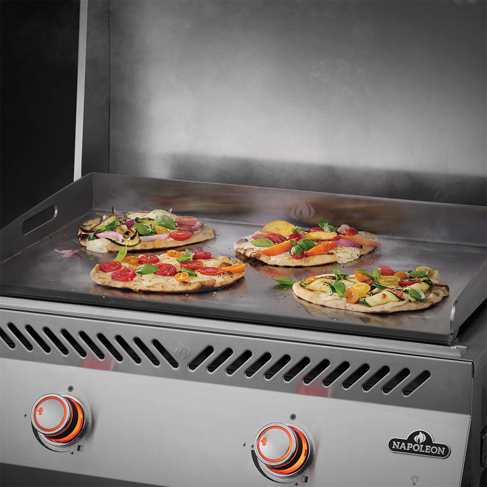 Flat top griddle cooking surface with pizza, peppers, and meats under the hood