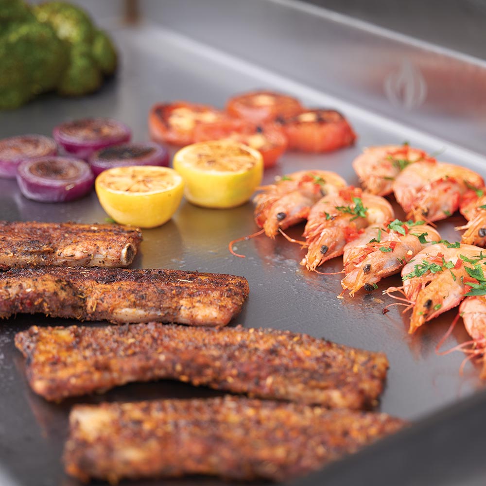 Close-up of food on a flat top griddle: grilled meats, peppers, and sliced onions