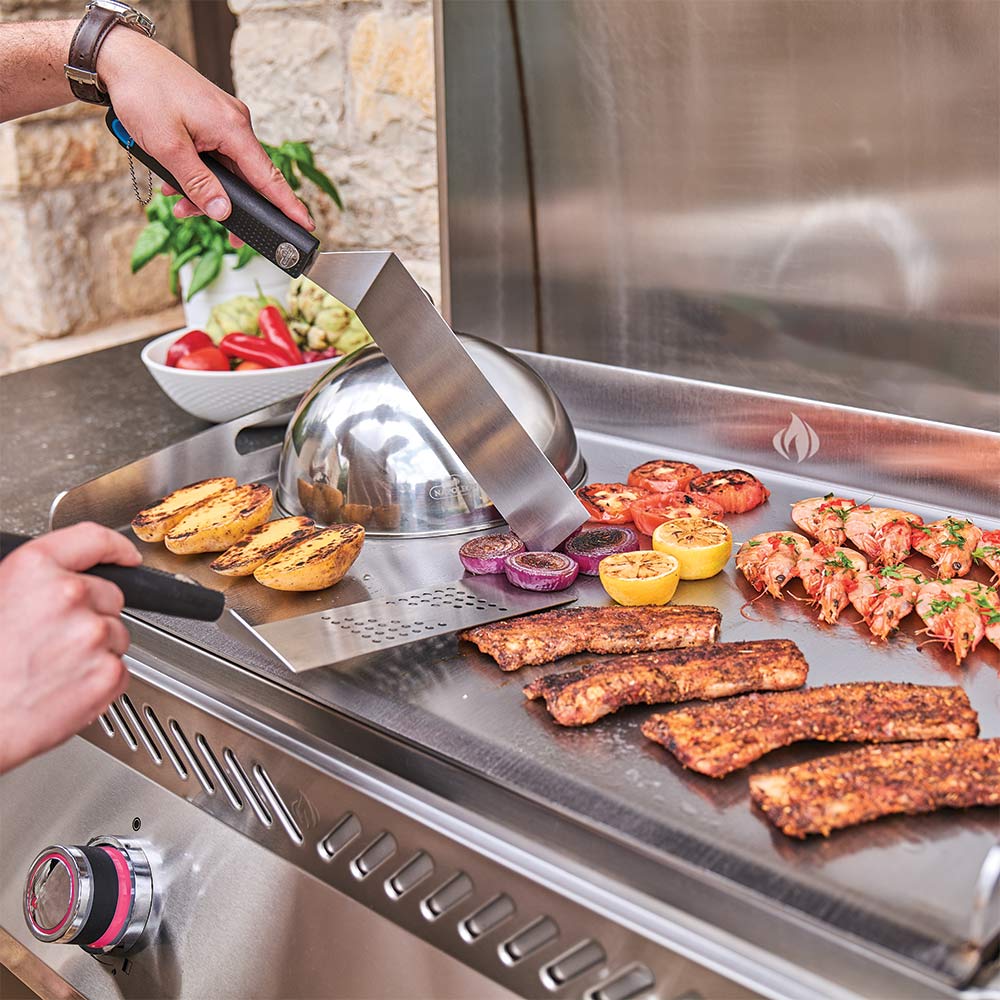 Flat top griddle being cooked on, with hands flipping food and vegetables on the surface