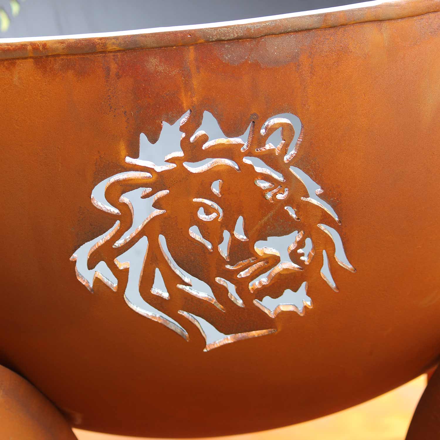 Orange steel fire pit bowl with bright lion head cutout and reflective metal edge.