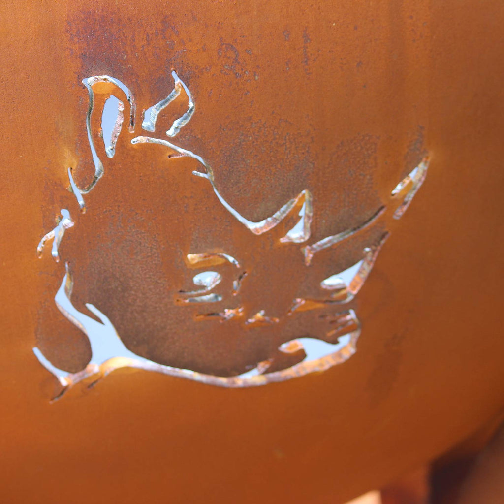 Orange steel fire pit bowl with animal head cutout and scattered perforation holes.