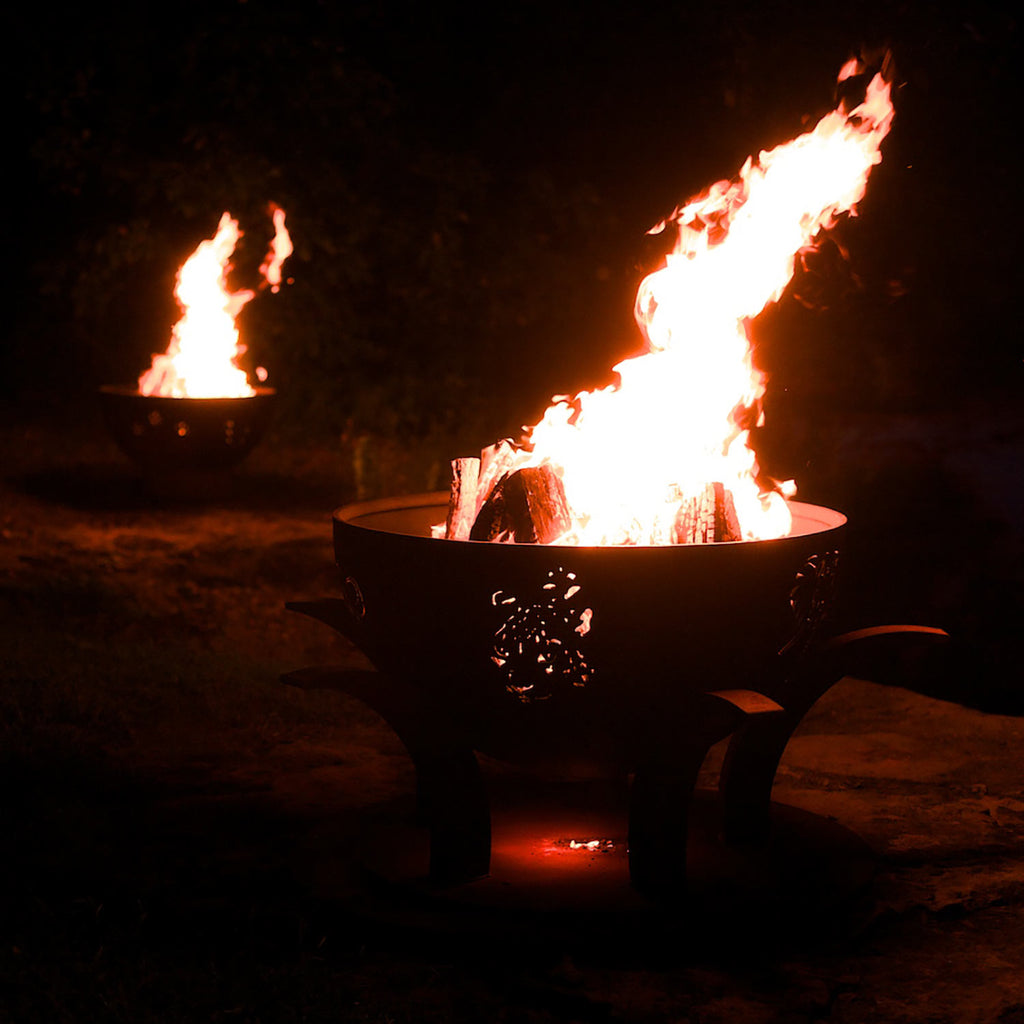 Wood fire pit burning with tall flames in a round black bowl and metal legs.