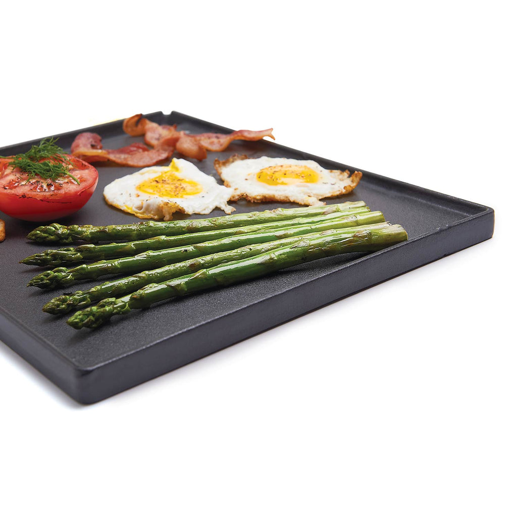 Cast iron griddle with grilled asparagus, fried eggs, and tomato halves on surface