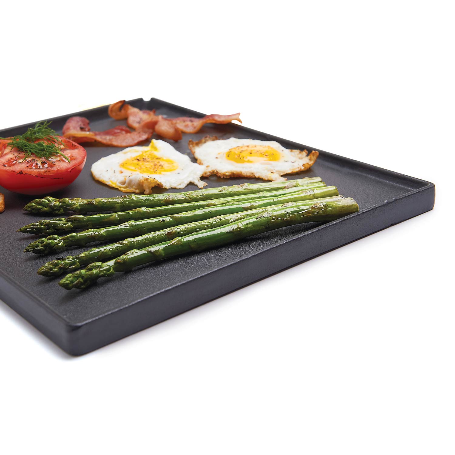 Cast iron griddle with grilled asparagus, fried eggs, and tomato halves on surface