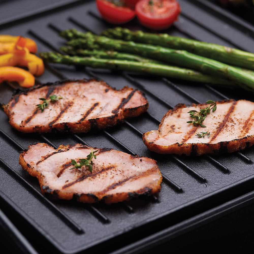 Cast iron griddle close-up with grilled meat slices, herbs, and asparagus spears