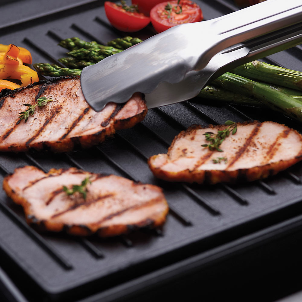 Cast iron griddle close-up with sliced meat, asparagus, and stainless spatula