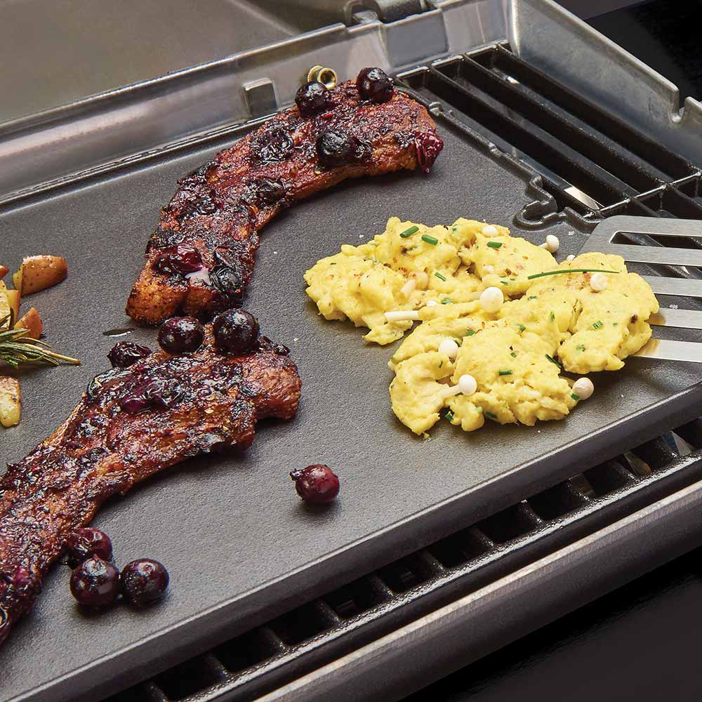 Cast iron griddle on grill grates, with cooked meat and scrambled eggs
