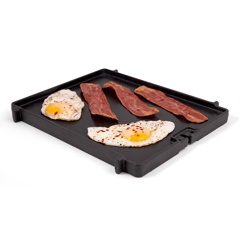 Cast iron griddle with sunny-side eggs and bacon strips on black surface