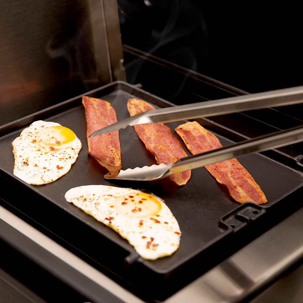 Cast iron side burner griddle plate with sunny-side eggs and bacon cooking